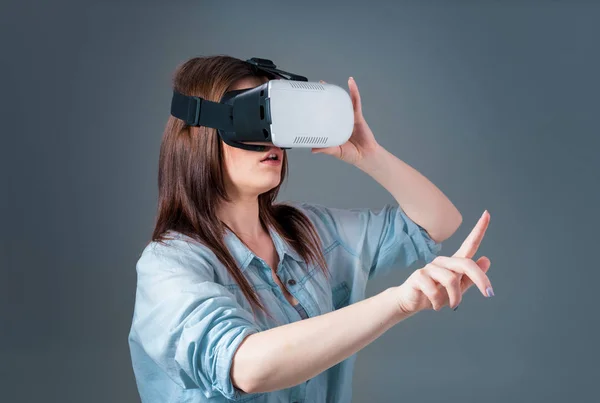 Giovane donna emotiva che utilizza un visore VR e sperimenta la realtà virtuale su sfondo grigio — Foto Stock