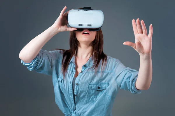 Giovane donna emotiva che utilizza un visore VR e sperimenta la realtà virtuale su sfondo grigio — Foto Stock