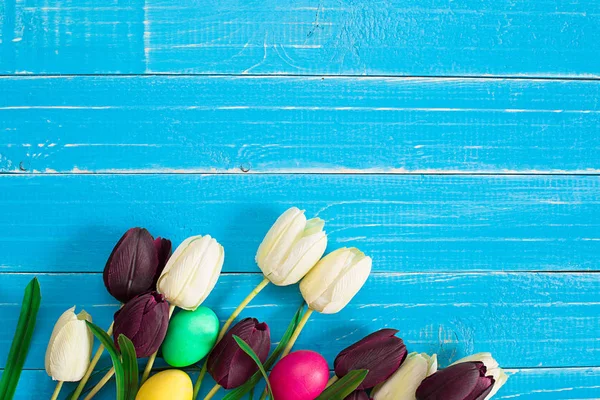 Bunte Ostereier und Tulpen auf blauem rustikalem Holzgrund — Stockfoto