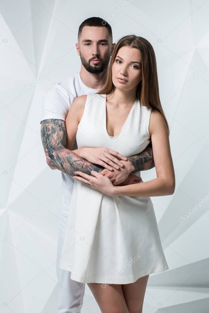 Young casual couple with woman holding his hands over womans shoulder and looking for the camera. On white background