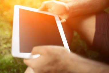 Kullanarak ve tablet bilgisayar yaz çim yazarak genç adam.