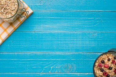 Mavi ahşap arka plan, üstten görünüm kaşık süt ve meyve bir kase ile yulaf gevreği