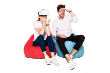 Beyaz arka plan üzerinde izole beanbags üzerinde oturmuş sanal gerçeklik gözlük karşılaşan arkadaş gülümseyen.