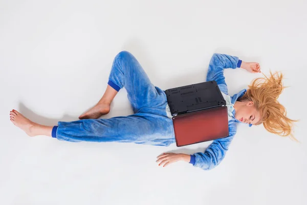 Ung kvinna liggande på golvet i sin pyjamas med en bärbar dator. — Stockfoto