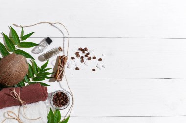 Doğal spa kahve çekirdekleri, tarçın, ayarla deniz tuzu, Hindistan cevizi yağı, kahverengi havlu ve Beyaz ahşap zemin üzerine yeşil yaprakları