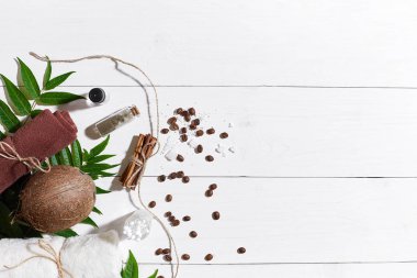 Doğal spa kahve çekirdekleri, tarçın, ayarla deniz tuzu, Hindistan cevizi yağı, kahverengi havlu ve Beyaz ahşap zemin üzerine yeşil yaprakları