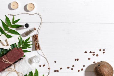 Doğal el yapımı kahve çekirdekleri, tarçın, sabunlar mumlar, Hindistan cevizi yağı, kahverengi havlu ve Beyaz ahşap zemin üzerine yeşil yaprakları