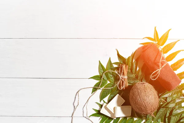 Natural handmade soaps with cinnamon, brown towel, coconut and green leaves on white wooden background. Sun flare — Stock Photo, Image