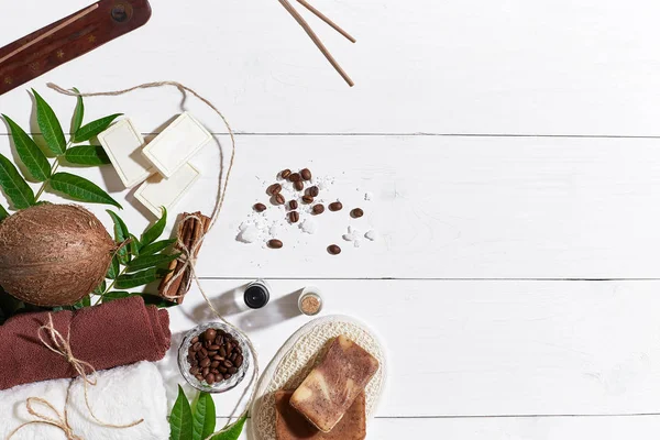 Natural handmade soaps with coffee beans, cinnamon, sea salt, loofah, brown towel, coconut and green leaves on white wooden background — Stock Photo, Image