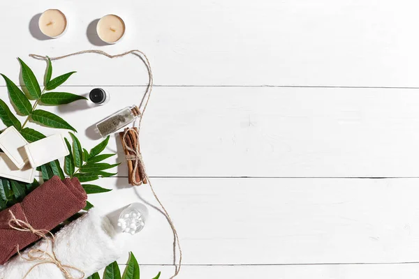 Natural handmade soaps with oil, cinnamon, candles, brown towel and green leaves on white wooden background — Stock Photo, Image