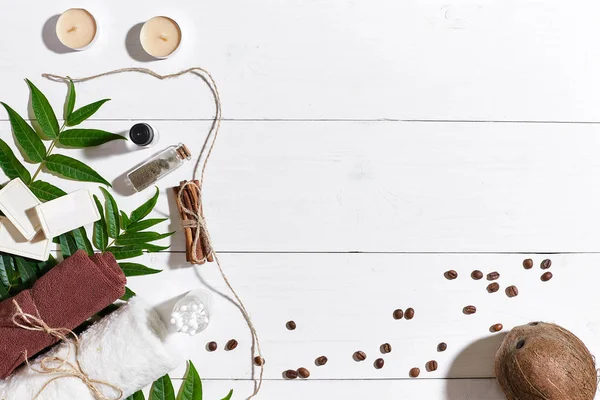 Doğal el yapımı kahve çekirdekleri, tarçın, sabunlar mumlar, Hindistan cevizi yağı, kahverengi havlu ve Beyaz ahşap zemin üzerine yeşil yaprakları