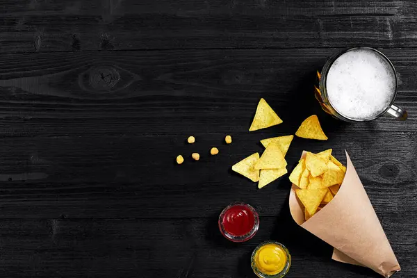Snack for party, chips, nachos with sauces: tomato ketchup , mustard and mug of beer on a black background. Top view, copy space — Stock Photo, Image