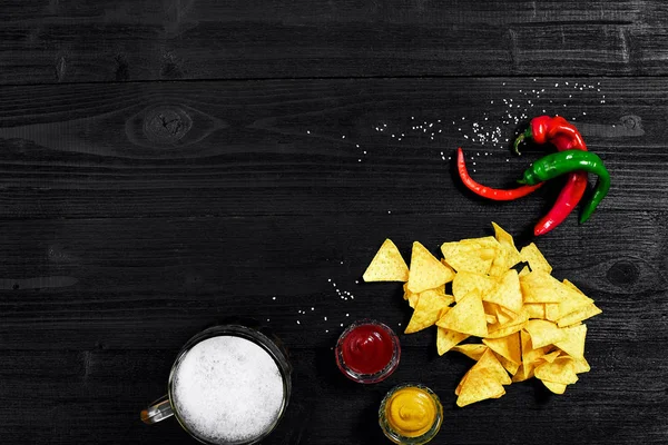 Snack para fiesta, patatas fritas, nachos con salsas: ketchup de tomate, mostaza y jarra de cerveza sobre fondo negro. Vista superior, espacio de copia — Foto de Stock