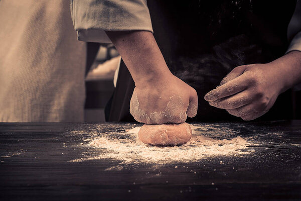 The chef makes dough for pasta on a wooden table