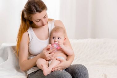 Anne ve çocuk beyaz bir yatakta. Anne ve bebek kız güneşli yatak odasında oynayan bebek bezi.