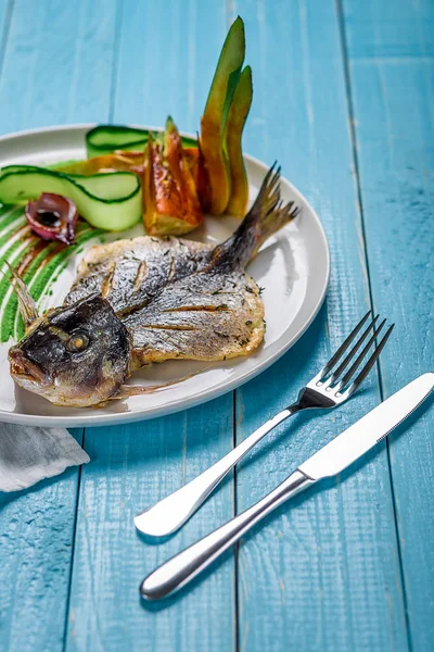 Dorado de poisson frit, décoré de concombres et d'oignons. Sur un fond en bois bleu — Photo