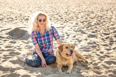 Güneş gözlüğü ile golden retriever köpek kum plajı üzerinde oturan genç güzel kadın portresi. Köpek deniz ile kız.