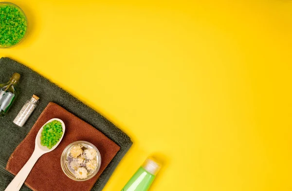 Spa or wellness setting in green colors. Bottles with essential aroma oil, towels, sea salt on yellow background. — Stock Photo, Image