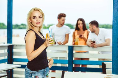 Sarışın kız bir barda bir yaz terasında kokteyl içecekler