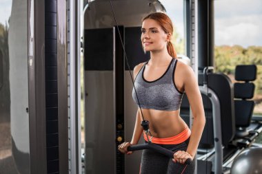 Spor salonundaki simülatörde egzersiz yapan kaslı genç kadın.