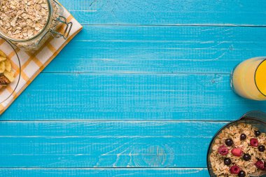 Mavi ahşap arka plan, üstten görünüm kaşık süt ve meyve bir kase ile yulaf gevreği