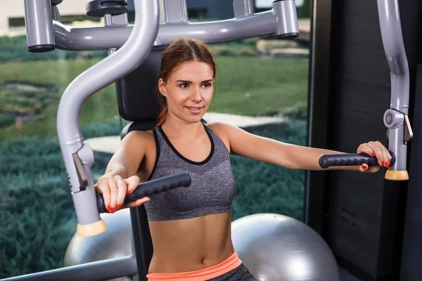 Mujer joven muscular haciendo ejercicios en el simulador en el gimnasio — Foto de Stock