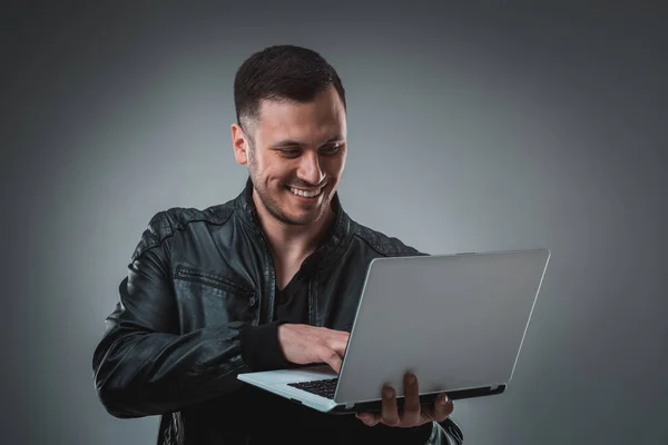 Mężczyzna w czarnej kurtce patrząc na laptopa, pół obrotu. Gospodarstwo otworzył laptopa i pracy. Emocje. — Zdjęcie stockowe