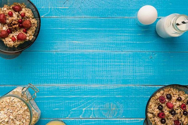 Oat flakes with milk and berries bowl with spoon on blue wooden background, top view — Stock Photo, Image