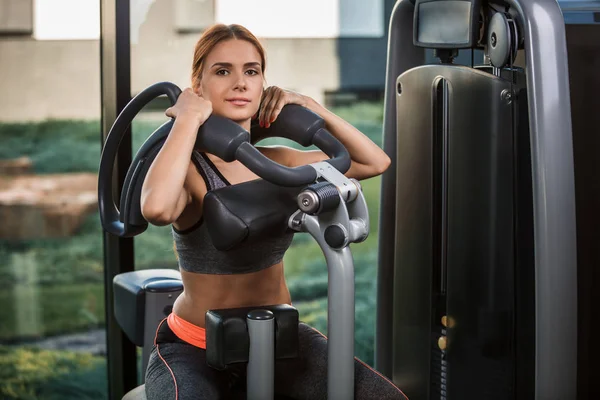 Mujer joven muscular haciendo ejercicios en el simulador en el gimnasio — Foto de Stock