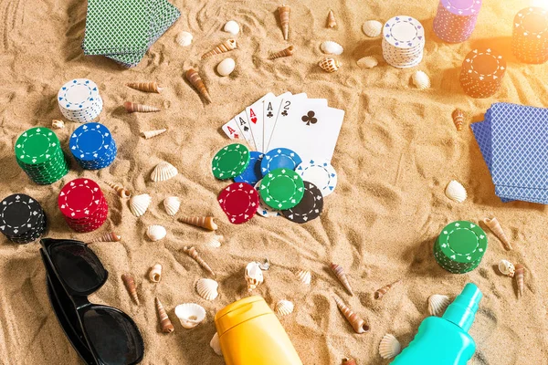 Tatil kavramı - beyaz kum deniz kabuklarını, renkli poker fişleri ve kartları ile kumar. Üstten Görünüm
