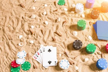 Tatil kavramı - beyaz kum deniz kabuklarını, renkli poker fişleri ve kartları ile kumar. Üstten Görünüm