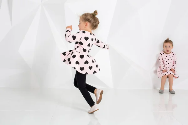 Két kis vicces, és nevetve a lány óvatosan rózsaszín ruha fehér stúdióban játszik — Stock Fotó
