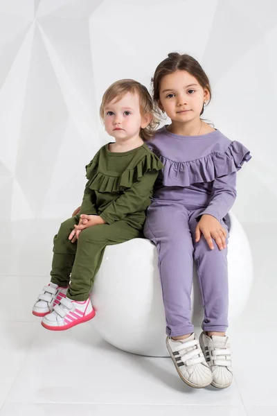 Дети, две сестры 1,5 и 5 лет в одинаковых костюмах разных цветов, маленькие девочки на белом фоне в студии — стоковое фото