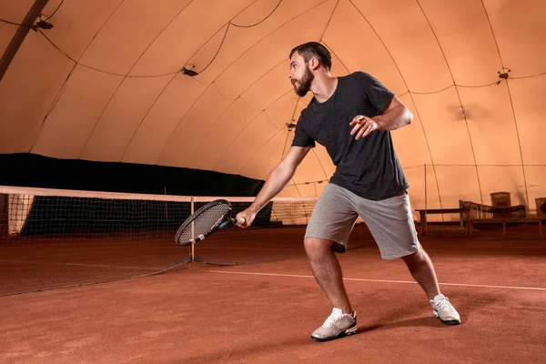 Beau jeune homme en t-shirt tenant une raquette de tennis sur un court de tennis — Photo