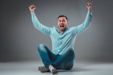 Gri arka plan üzerinde izole kaldırdı elleriyle bir katta oturan yakışıklı genç adam