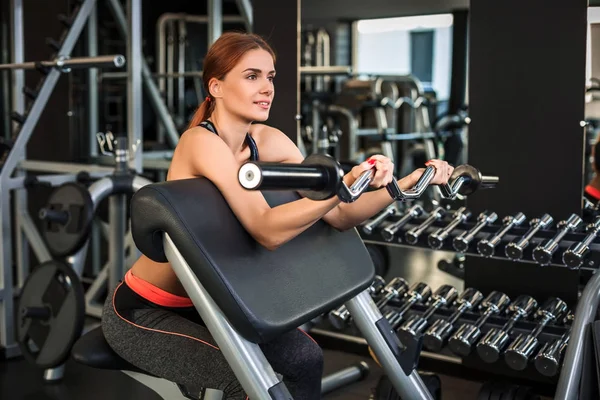 Spor salonundaki simülatörde egzersiz yapan kaslı genç kadın.