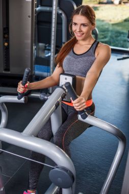 Spor salonundaki simülatörde egzersiz yapan kaslı genç kadın.