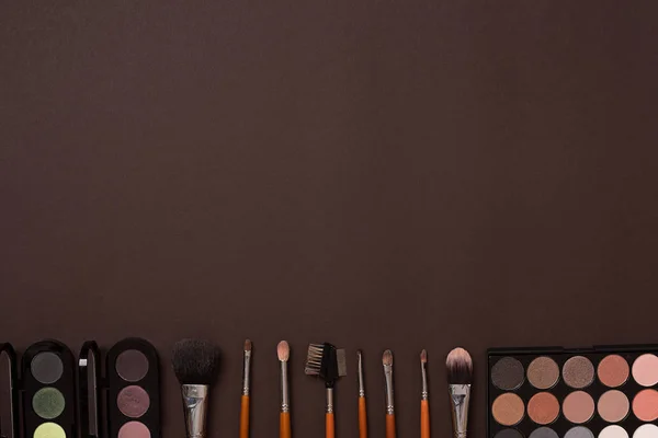Varios cosméticos y pinceles sobre fondo marrón — Foto de Stock