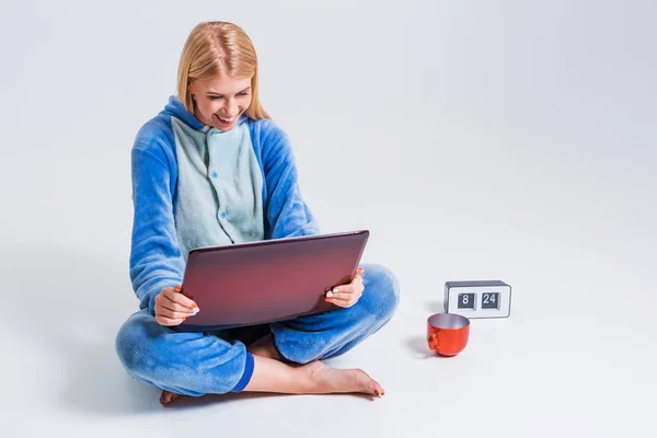 Молода жінка сидить на підлозі в піжамі з ноутбуком . — стокове фото
