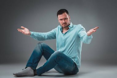 Gri arka plan üzerinde el hareketi kaldırdı elleriyle bir katta oturan yakışıklı genç