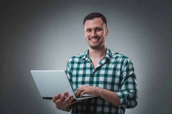 Ελκυστικό επιχειρηματικό μοντέλο άνθρωπος σε πράσινο πουκάμισο που απομονώνονται σε γκρι λειτουργεί με laptop, δείχνοντας κάτι με το αριστερό χέρι. — Φωτογραφία Αρχείου