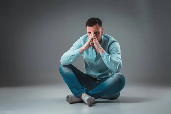 Der Mann sitzt auf dem Boden, isoliert auf grauem Hintergrund. Mann zeigt andere Emotionen. — Stockfoto