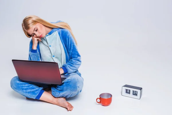 Jovem sentada no chão de pijama com um laptop . — Fotografia de Stock