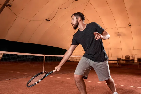 Beau jeune homme en t-shirt tenant une raquette de tennis sur un court de tennis — Photo