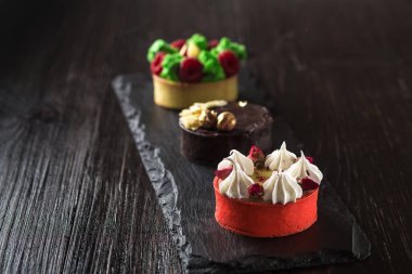 Yan görünümü üzerinde mini parti tartlets taze meyve, çikolata, fındık ve siyah arduvaz arka plan üzerine krem