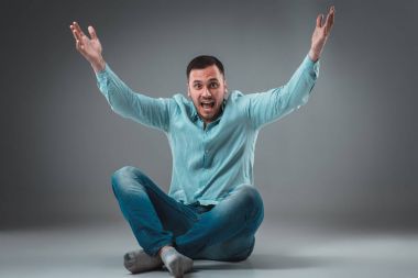 Adam gri arka plan üzerinde katta oturuyor. Adam gösteren farklı duygular.