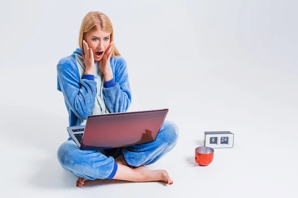 Ung kvinna sitter på golvet i sin pyjamas med en bärbar dator. — Stockfoto