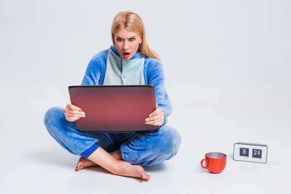 Ung kvinna sitter på golvet i sin pyjamas med en bärbar dator. — Stockfoto