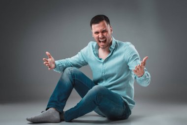 Adam gri arka plan üzerinde izole katta oturuyor. Adam gösteren farklı duygular.