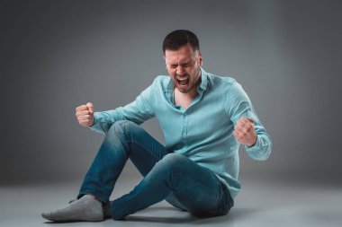 Adam gri arka plan üzerinde izole katta oturuyor. Adam gösteren farklı duygular.